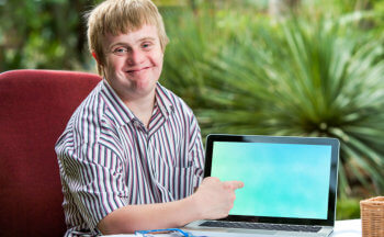 Friendly boy with down syndrome pointing at blank laptop screen